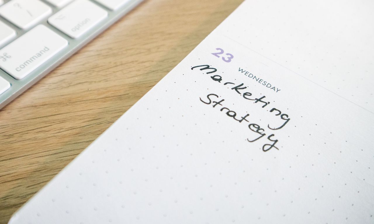 Close-up of a planner with Marketing Strategy handwritten alongside keyboard.
